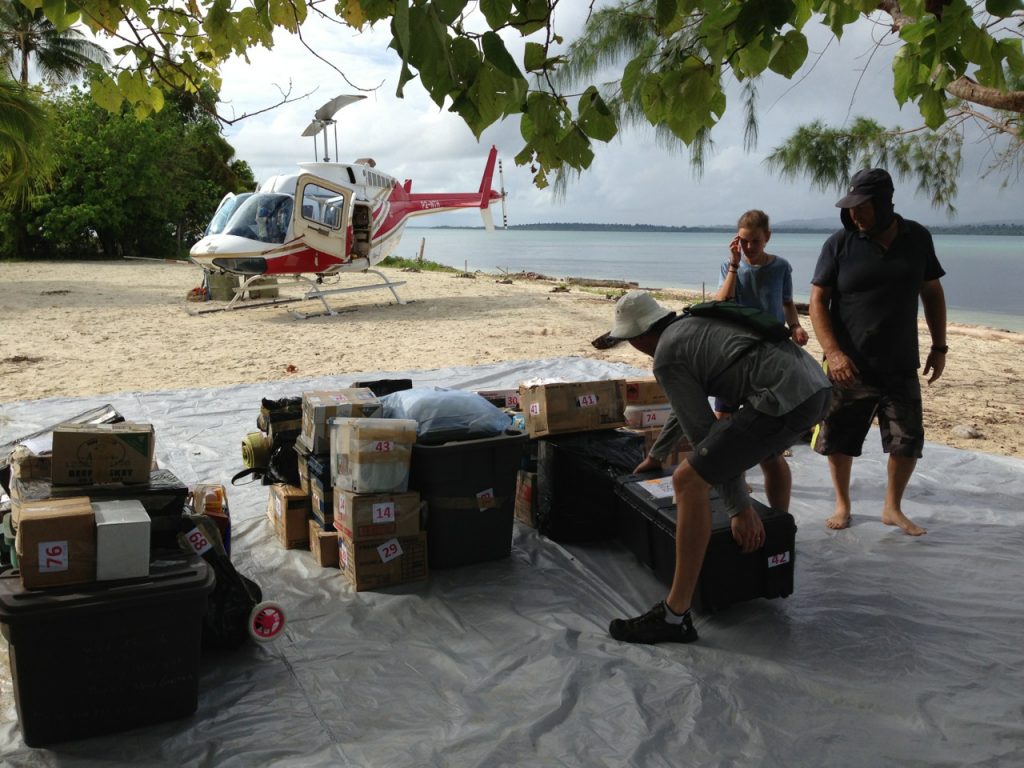 missionaries organize cargo on a beach with helicopter in the background