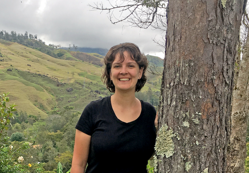 Kristen standing by a tree with a Papua New Guinea mountain valley in the background