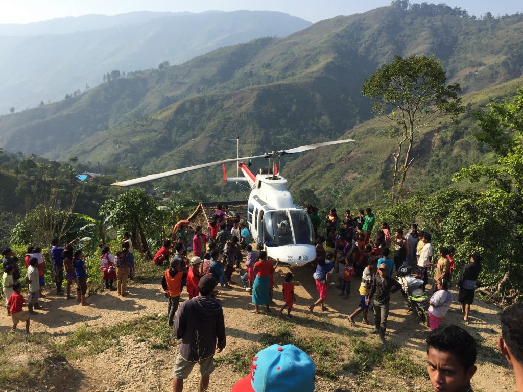 villagers gathered around the helicopter on a remote, mountainside landing-pad